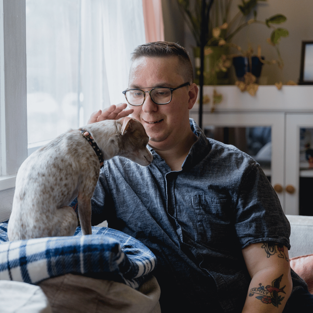 CHIRYO Outcomes and Intervention Services man with family tattoo sat on sofa engaging petting dog