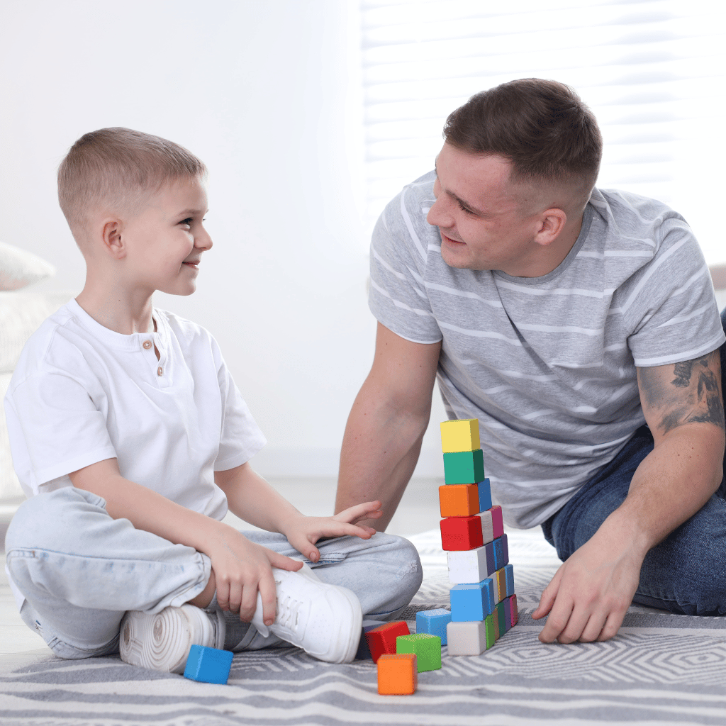 CHIRYO Outcomes and Intervention Services sat on floor eith son stacking building blocks smiling at each another